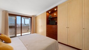 A bedroom with a bed, a wardrobe, a television on a shelf, and a view through a glass door. - AgoRattico – Elegant Penthouse with Panoramic Terrace (Quartu Sant'Elena)