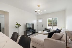 Ein modernes Wohnzimmer mit Flachbildfernseher, einem Esstisch und einer Couch.