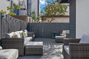 Eine Terrass mit Korbmöbeln, einem Holzdeck und einem grauen Zaun.