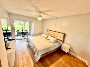 A bedroom with a bed, a desk, and a chair. There is a sliding glass door leading to an outdoor area. - Snowbird Escape: Turnkey 2BR Naples Condo with Golf Views & Screened Lanai (Naples)
