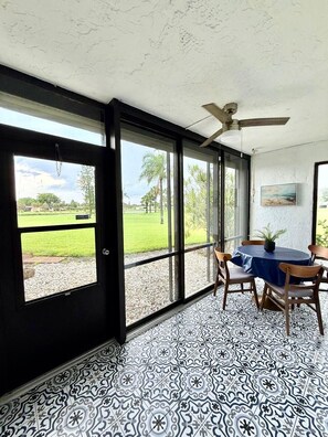 A room with a large window, a ceiling fan, a table with chairs, and a patterned floor. - Snowbird Escape: Turnkey 2BR Naples Condo with Golf Views & Screened Lanai (Naples)