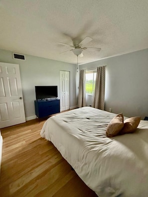 A bedroom with a bed, a ceiling fan, a television, and a window with curtains. - Snowbird Escape: Turnkey 2BR Naples Condo with Golf Views & Screened Lanai (Naples)
