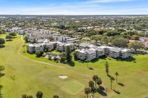A residential area with apartment buildings, green lawns, and a golf course. - Snowbird Escape: Turnkey 2BR Naples Condo with Golf Views & Screened Lanai (Naples)
