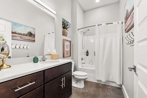A modern bathroom with a white sink, dark wooden cabinets, a toilet, a shower with a glass door, and a painting on the wall. - Library Retreat | Antiques & Gallery Wall (Nashville)