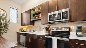 A modern kitchen with dark wooden cabinets, stainless steel appliances, and a built-in oven. - Library Retreat | Antiques & Gallery Wall (Nashville)