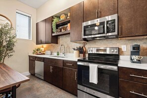 A modern kitchen with dark wooden cabinets, stainless steel appliances, and a built-in oven. - Library Retreat | Antiques & Gallery Wall (Nashville)