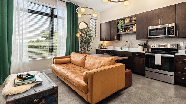 A modern kitchen with dark cabinets, stainless steel appliances, and a dining area with a leather sofa and a small table. - Library Retreat | Antiques & Gallery Wall (Nashville)