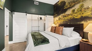 A bedroom with a bed, a nightstand, a lamp, a painting on the wall, and a sliding closet door. - Library Retreat | Antiques & Gallery Wall (Nashville)
