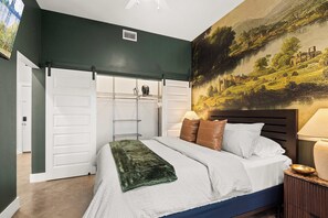 A bedroom with a bed, a nightstand, a lamp, a painting on the wall, and a sliding closet door. - Library Retreat | Antiques & Gallery Wall (Nashville)