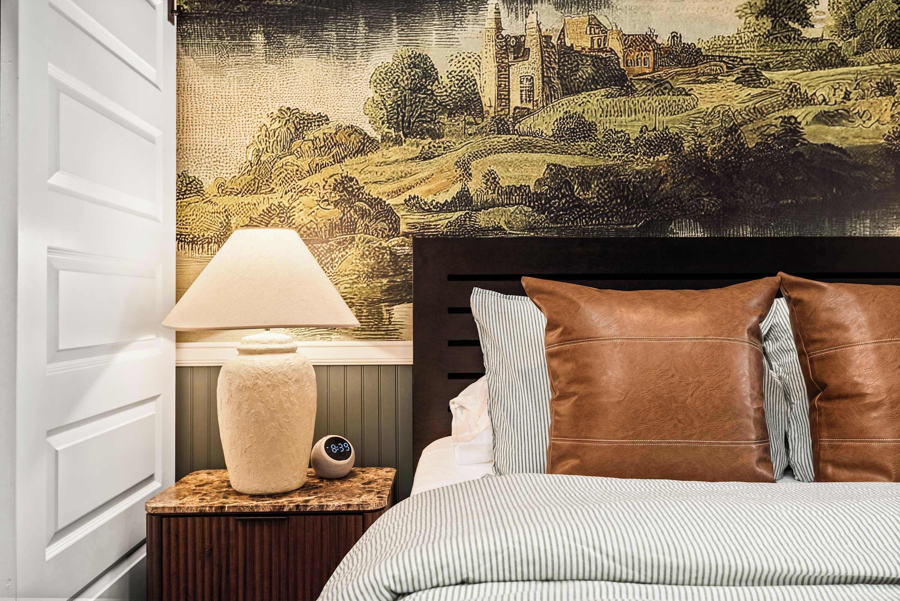 Un dormitorio con cama, una mesita de noche con lámpara y un cuadro de paisaje en la pared.