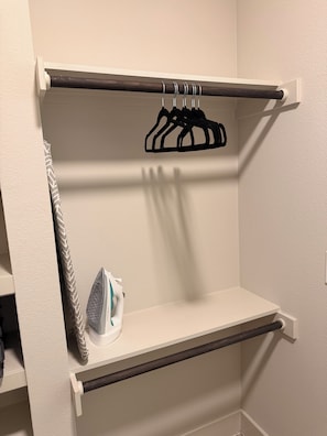 A closet with a hanging rack, an ironing board, and a shelf. - Skyline Balcony Retreat | Luxury Apartment | Pool (Dallas)