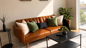 Ein modernes Wohnzimmer mit einem braunen Ledersofa, einem schwarzen Couchtisch und einem großen Fenster mit Blick auf die Stadt.