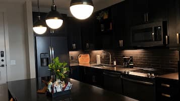 A modern kitchen with dark cabinetry, a central island, stainless steel appliances, and pendant lighting.