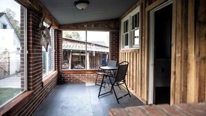 Eine überdachte Veranda mit einer Ziegelmauer, einem Tisch mit Stühlen und einem Fenster, das auf einen Garten blickt.