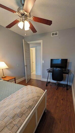 A bedroom with a bed, a desk with a chair, a ceiling fan, and a television. - Bentonville Basecamp Bike-Friendly Near Downtown & Crystal Bridges (Bentonville)