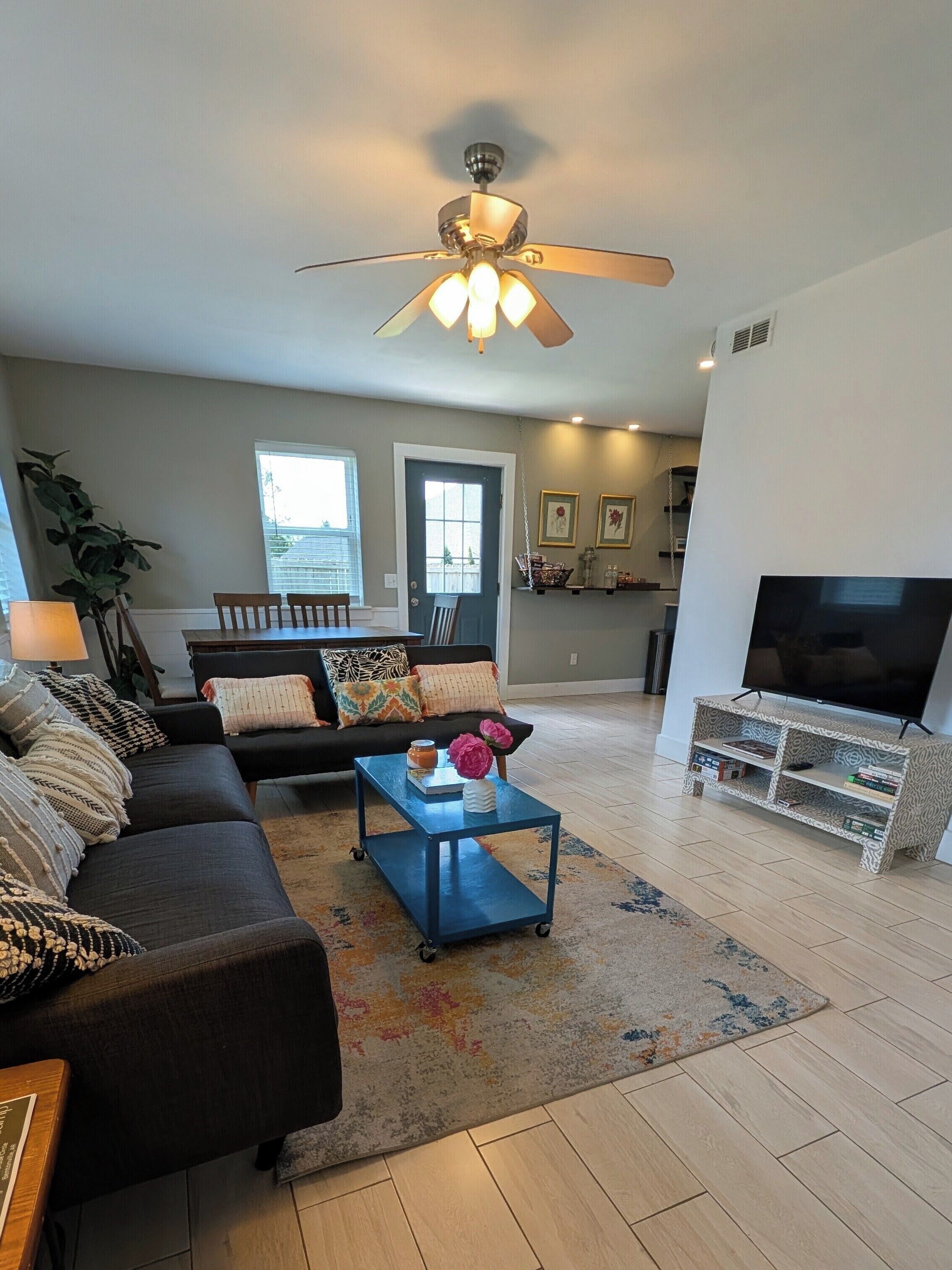 A living room with a sofa, coffee table, TV stand, and ceiling fan.