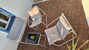 Ein Patio mit Pflasterboden, Metallstühlen und einem kleinen Tisch mit einer grünen Flasche.