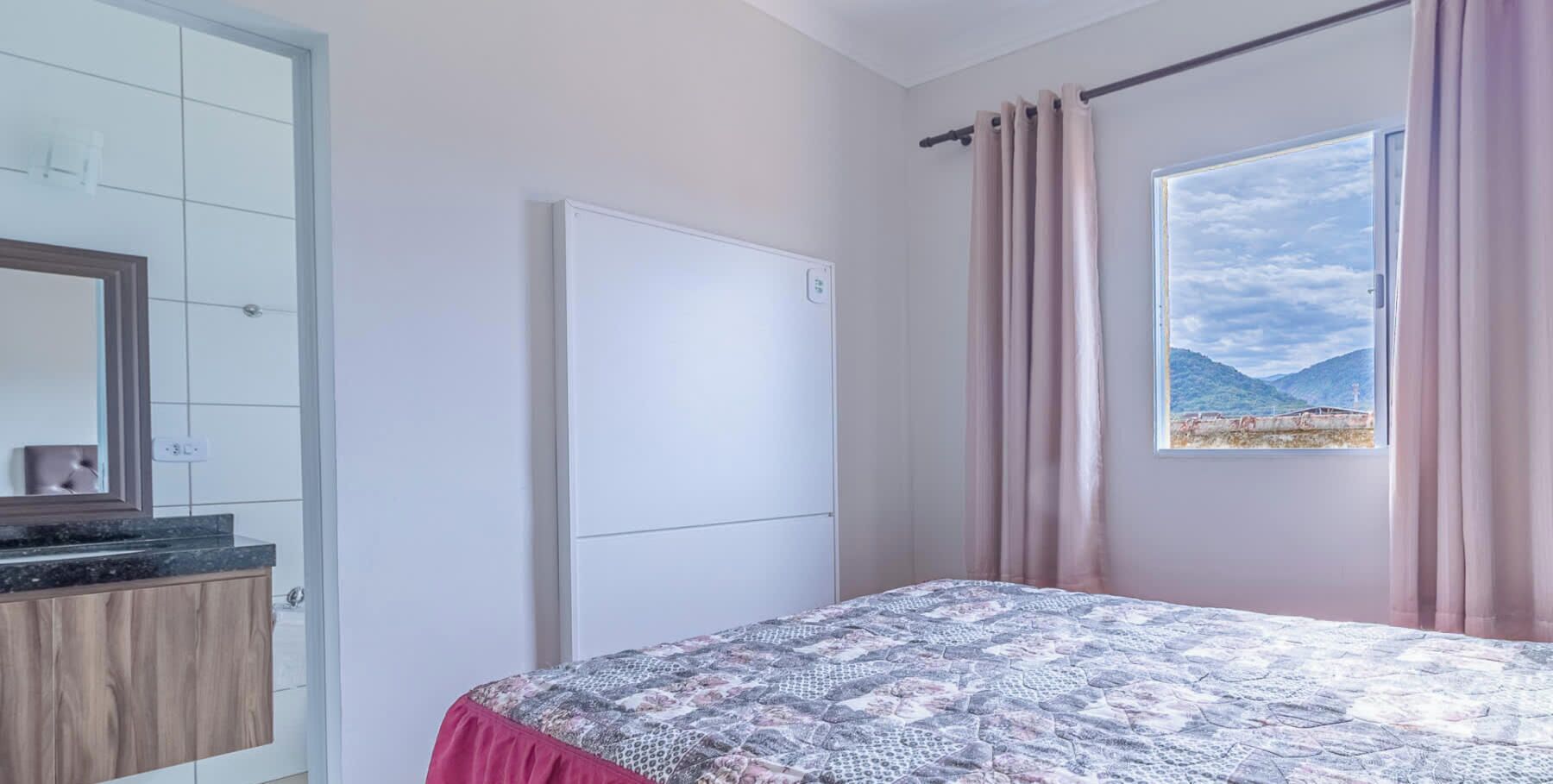 A bedroom with a bed, a window with a view, a door, and a mirror.