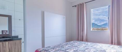 A bedroom with a bed, a window with a view, a door, and a mirror.