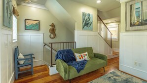 A room with a green sofa, a blue chair, wooden flooring, a staircase, and wall art. - Cozy Condo with River views (Carrabelle)