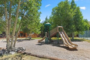 Ein Spielplatz mit Rutschen und Klettergerüsten, umgeben von Bäumen und einer Kiesfläche.