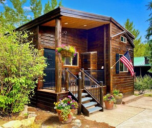 A wooden cabin with a porch, a flag, and potted plants.