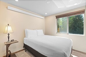 A bedroom with a bed, a nightstand, a lamp, and a window with a view of trees. - 2-bed, 2 Bath Tiger Run chalet in charming Breckenridge with cozy mountain vibes (Breckenridge)