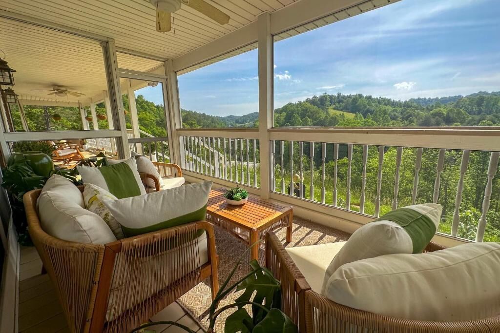 A covered porch with wicker furniture, a small table, and a view of a forested landscape.