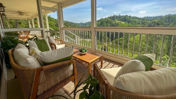 A covered porch with wicker furniture, a small table, and a view of a forested landscape. - Munaya Resort (Marshall)