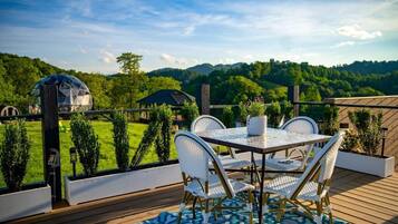 An outdoor deck with a table and chairs, overlooking a green landscape.