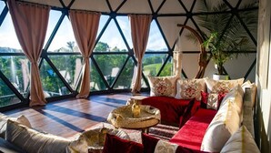 A room with a high ceiling, large windows, a red sofa, and a decorative wall hanging. - Munaya Resort (Marshall)