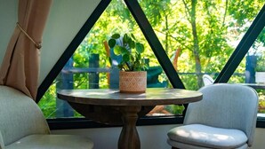 A room with a round table, two chairs, a potted plant, and a view of greenery through a window. - Munaya Resort (Marshall)