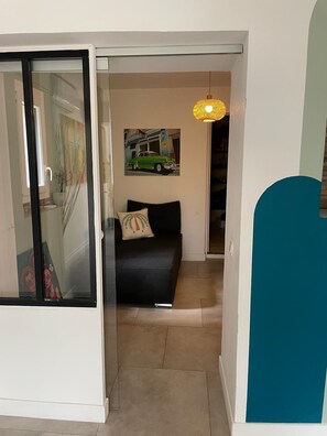 Ein schmaler Flur mit einer Schiebetür zu einem Raum, der ein schwarzes Sofa und ein Gemälde einer grünen Limousine an der Wand zeigt.