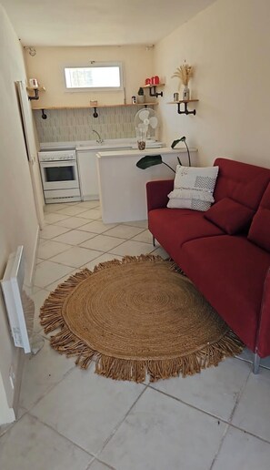 Ein Wohnzimmer mit einem roten Sofa, einem gewebten Teppich, einer Küche im Hintergrund und einem Fenster.