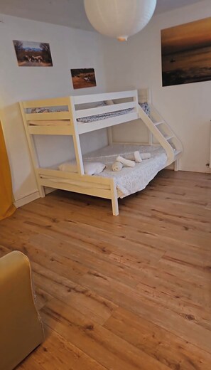 Ein Stockbett mit Holzrahmen und einer weißen Matratze, Holzboden und weiße Decke mit einer Pendelleuchte.