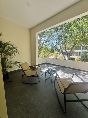 Ein Balkon mit zwei Stühlen, einem kleinen Tisch, einem Blumentopf und Blick auf Bäume und Gebäude.