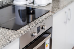 A kitchen with a built-in induction cooktop and a stainless steel oven. - GuestReady - Dream Corner (Caniço)