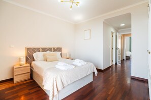 A hotel room with a large bed, bedside tables, a modern chandelier, and a wooden floor. - GuestReady - Dream Corner (Caniço)