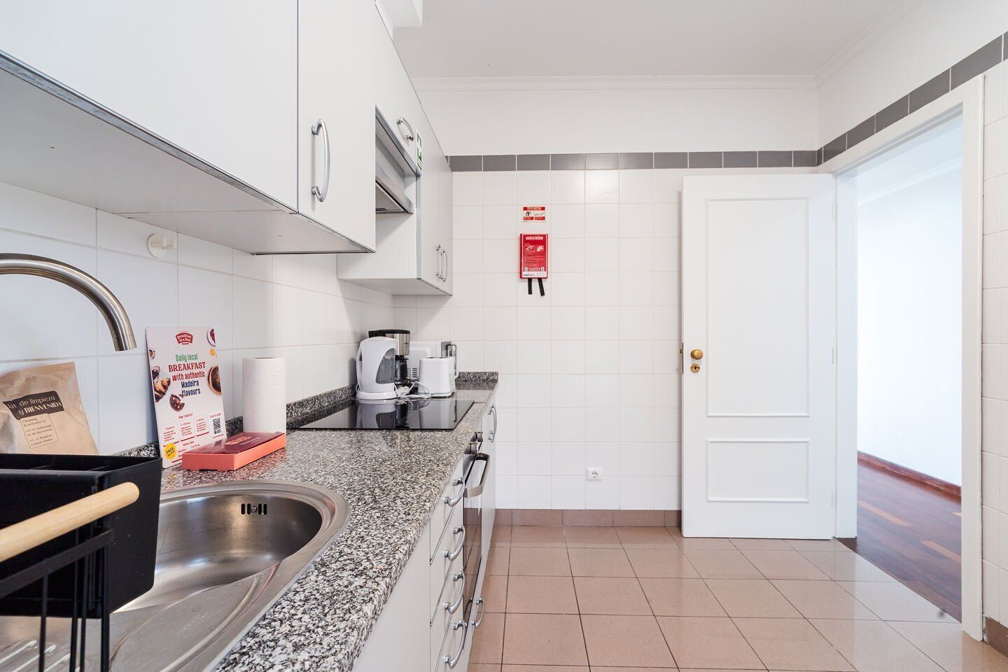 A modern kitchen with a granite countertop, stainless steel sink, and a coffee machine.