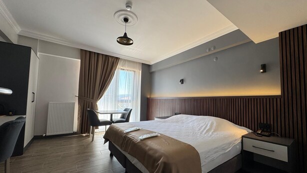 A hotel room with a bed, bedside table, desk, chair, and a window with curtains. - The Liora Hotel (Boyabat)