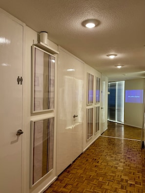 Un pasillo con puertas blancas, suelo de madera e iluminación empotrada en el techo.
