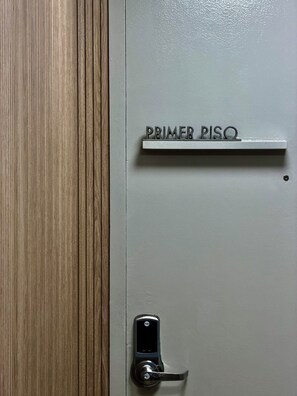 Una puerta con una cerradura Yale y una placa metálica encima que dice 'PRIMER PISO'.