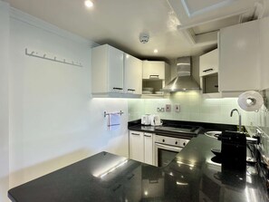 A modern kitchen with white cabinets, a black countertop, a stainless steel range hood, and a coffee machine. - South Ken Rooftop Loft  Treetop Views  Hyde Park (London)
