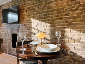 A dining table set with plates, cutlery, and glasses, with a brick wall and a flat-screen TV in the background. - South Ken Rooftop Loft  Treetop Views  Hyde Park (London)