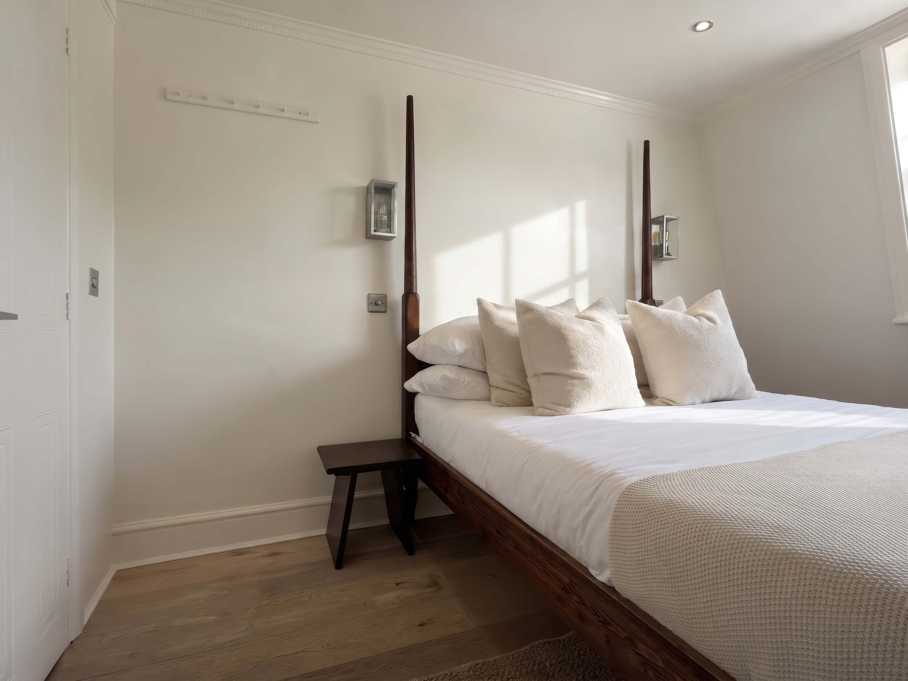 A bedroom with a wooden bed frame, white bedding, a small bedside table, and a nightstand.