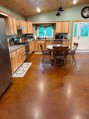 A kitchen with wooden cabinets, a dining table with chairs, a refrigerator, and a clock on the wall. - Welcome to Bud and Jacquie Sue’s (Sterling)