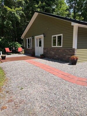 A single-story building with a gravel driveway leading to a front door, two windows, and a small porch area with red chairs. - Welcome to Bud and Jacquie Sue’s (Sterling)