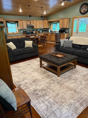 A spacious living room with dark sofas, a wooden coffee table, and a large rug. - Welcome to Bud and Jacquie Sue’s (Sterling)