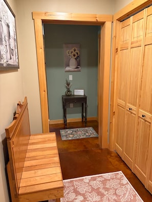A wooden bench, a small table with a vase and a welcome sign, and a wooden wardrobe in a room with a green wall and a wooden floor. - Welcome to Bud and Jacquie Sue’s (Sterling)