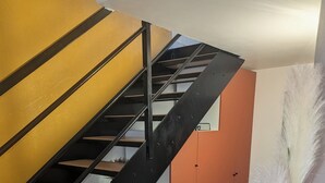 Una scala con ringhiera in metallo nero, gradini in legno e parete gialla.